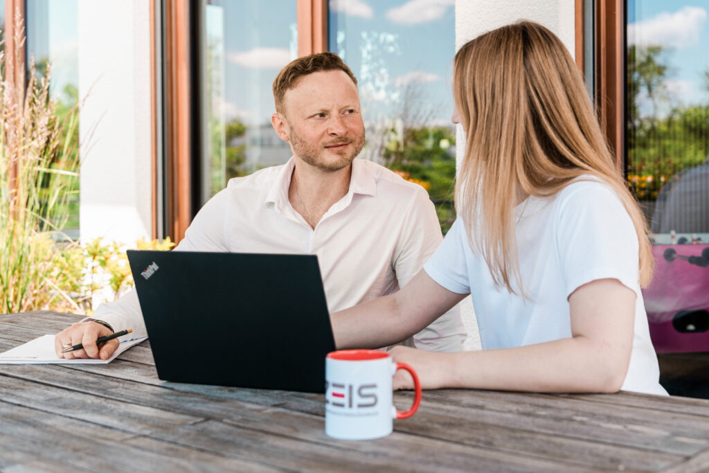 Florian Zeis und eine Kollegin besprechen gemeinsam Unterlagen am Laptop.