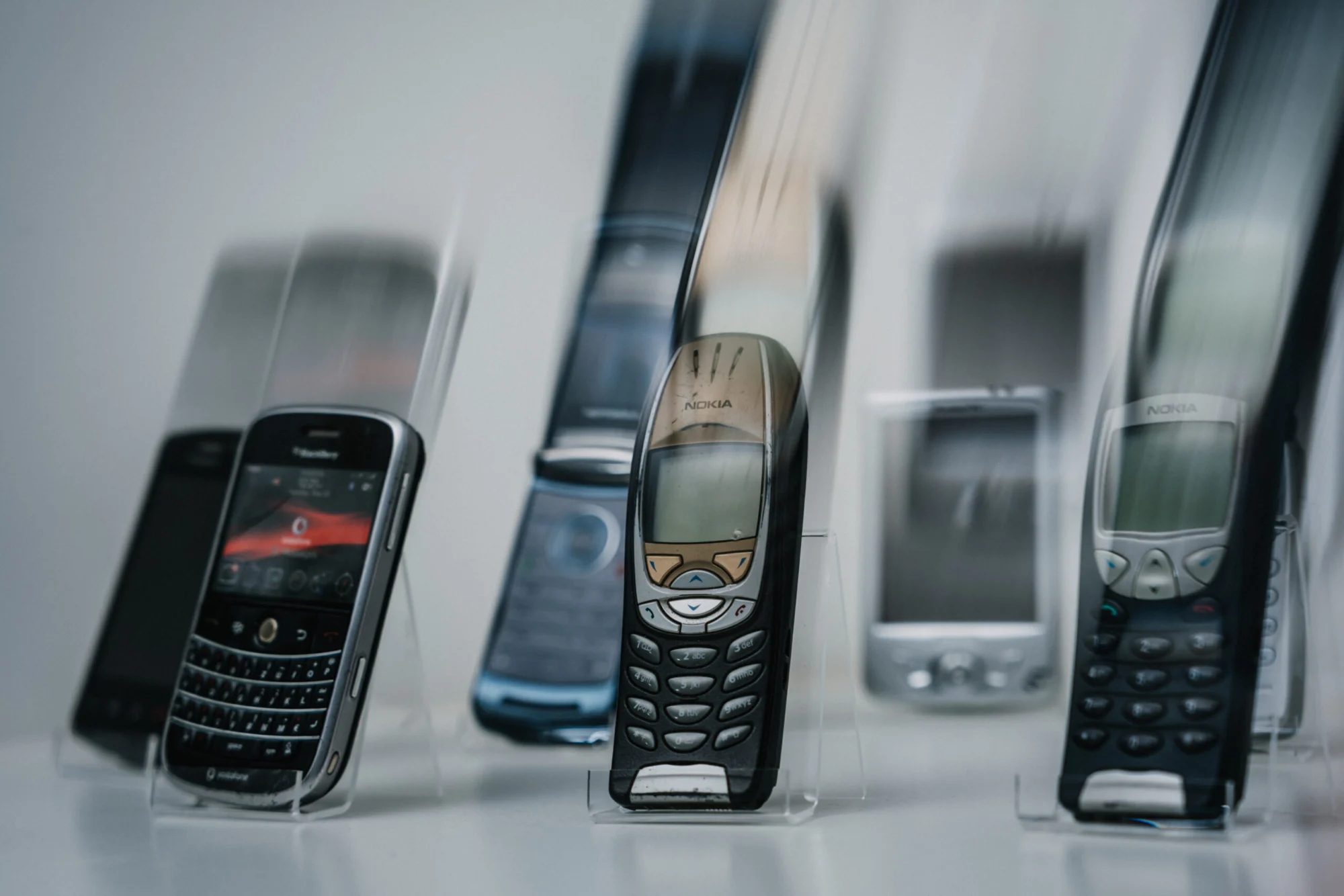 Sammlung &auml;lterer Mobiltelefone, darunter BlackBerry und Nokia, auf transparenten St&auml;ndern