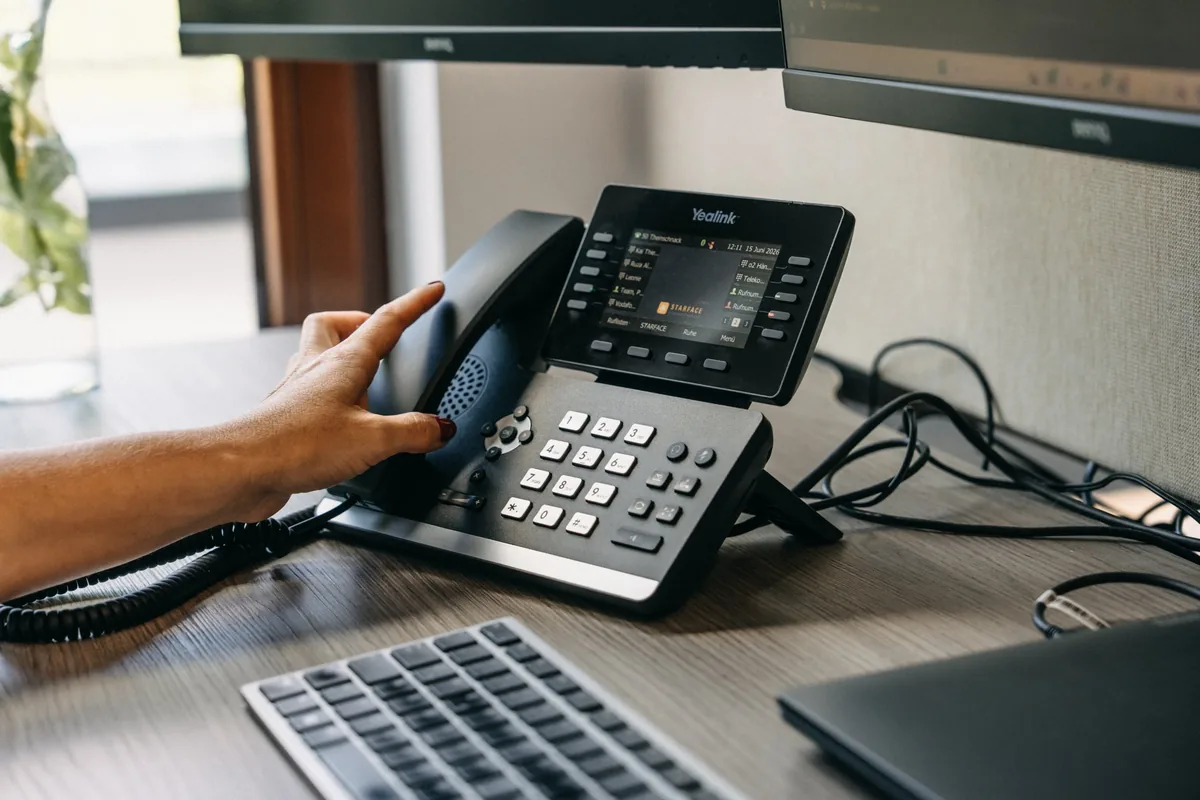 Business-Tischtelefon am Arbeitsplatz: Eine Hand greift zum H&ouml;rer.