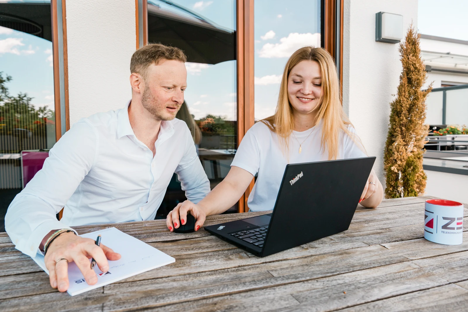 Zwei Personen arbeiten gemeinsam an einem Laptop auf der Terrasse.
