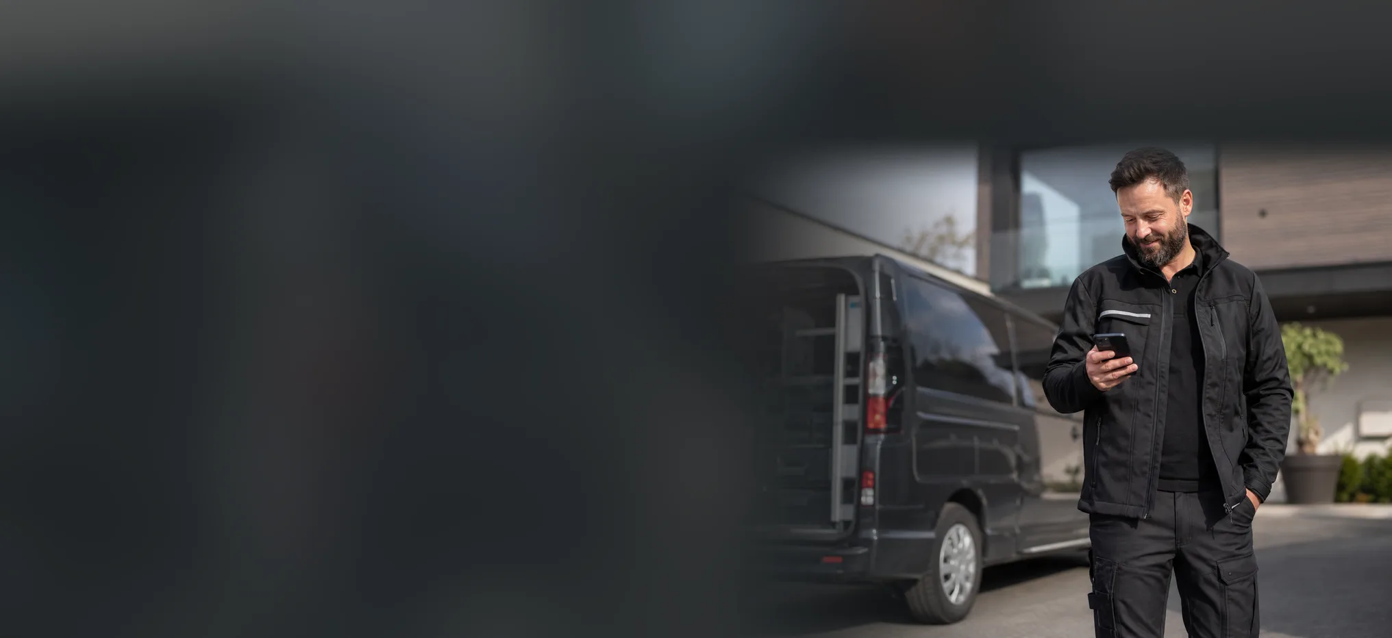 Handwerker mit Smartphone vor seinem Firmentransporter